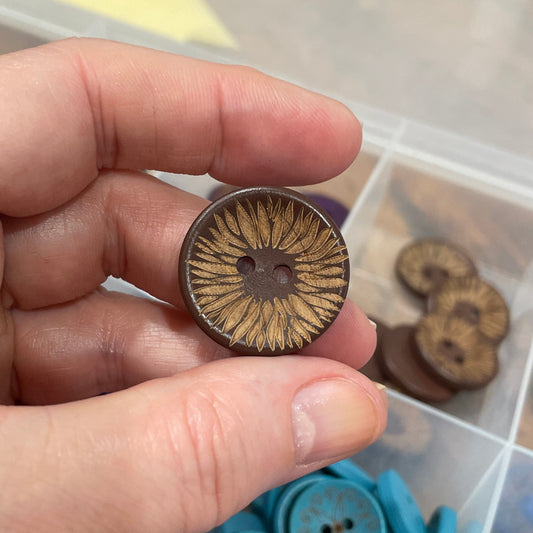 Hand holding a brown button with a container of various buttons in the background