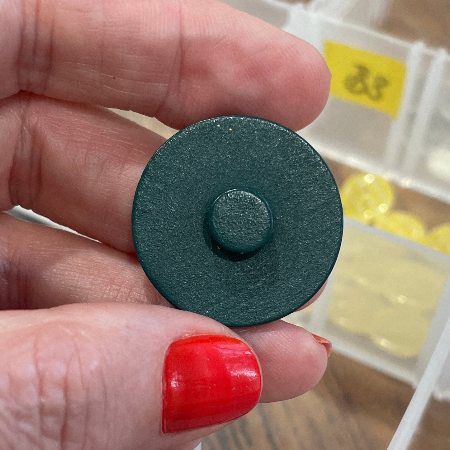 Hand holding a button in front of a button organizer with various buttons.