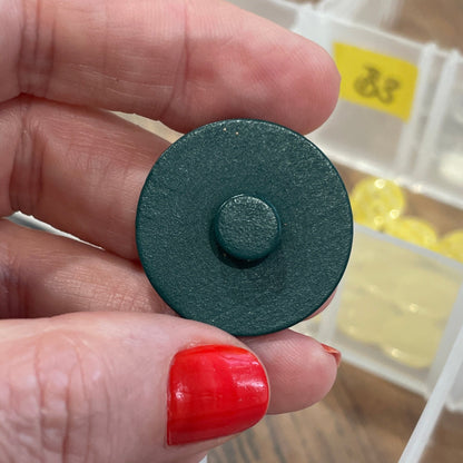 Hand holding a button in front of a button organizer with various buttons.