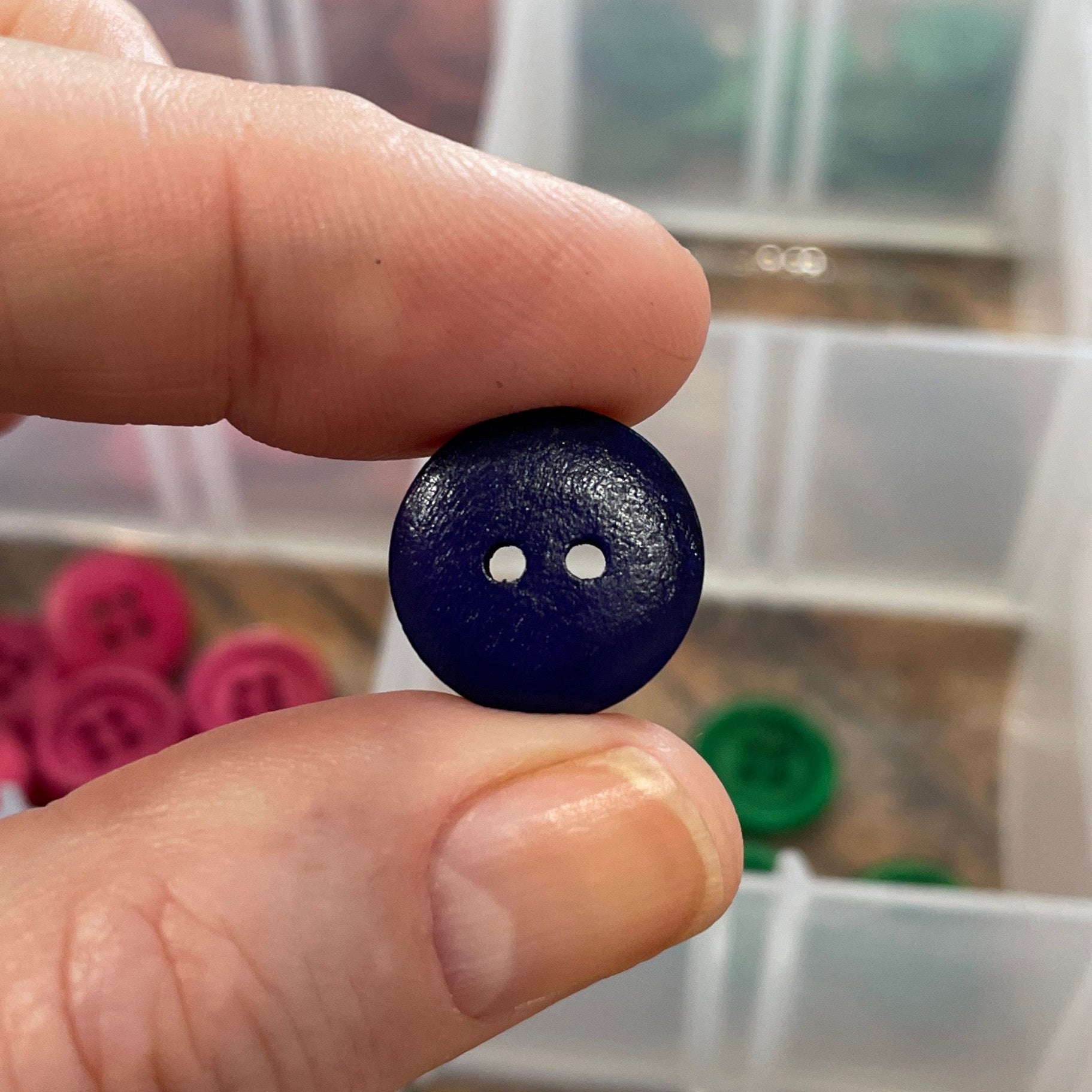 Person holding a button with white dots in front of a container of buttons.