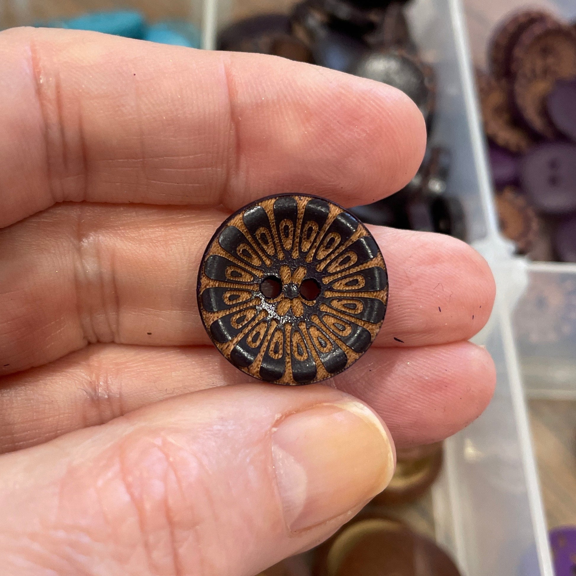 Hand holding a decorative button with a collection of buttons in the background.