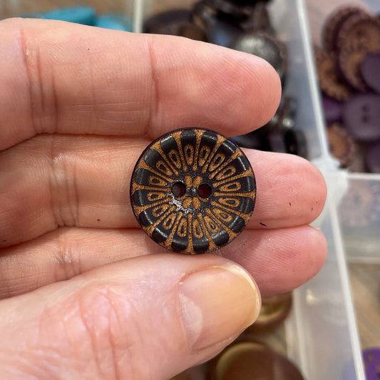 Hand holding a decorative button with a collection of buttons in the background.