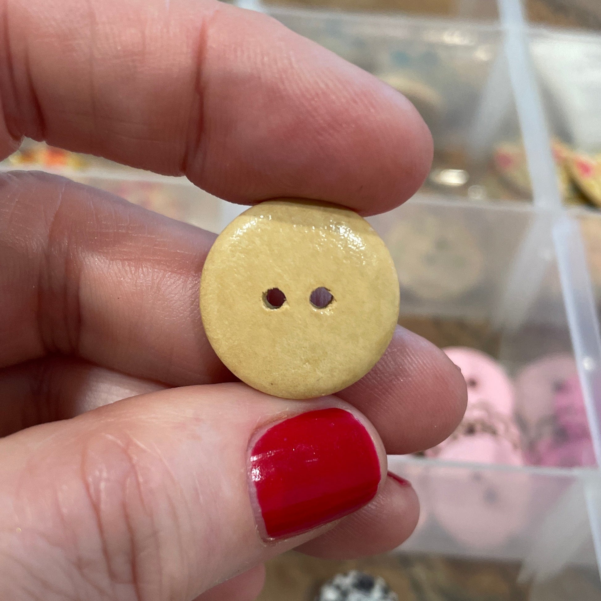Hand holding a yellow button with a blurred background of a container with buttons