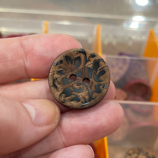 Hand holding a decorative button with a background of various buttons in a case.