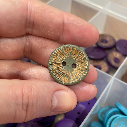 Hand holding a gold button with a container of assorted buttons in the background