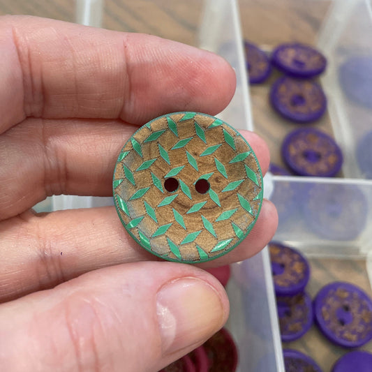 Hand holding a decorative button with a background of button assortment