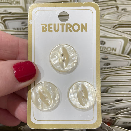 Set of pearl-like buttons on a Beutron card held by a hand with red nail polish.