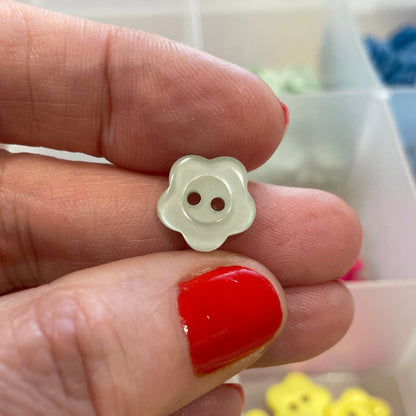 Hand holding a white flower-shaped button with a blurred background of a container with buttons.