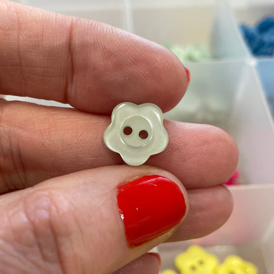Hand holding a white flower-shaped button with a blurred background of a container with buttons.