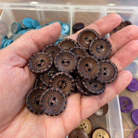 Hand holding a collection of brown buttons with a blurred background of more buttons.