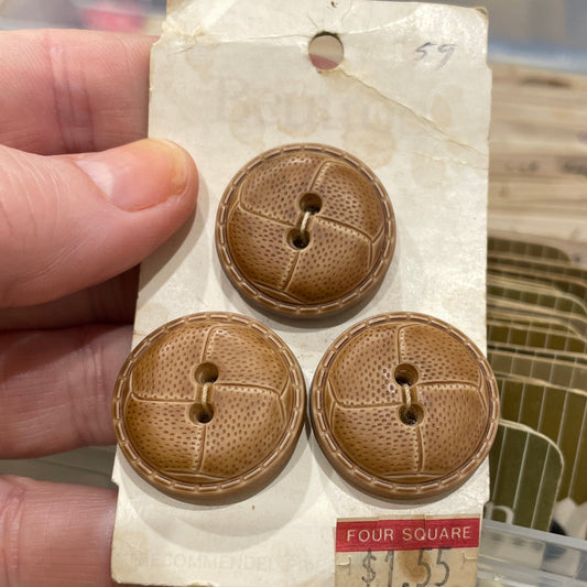 Three brown buttons on a card held by a hand with a blurred background