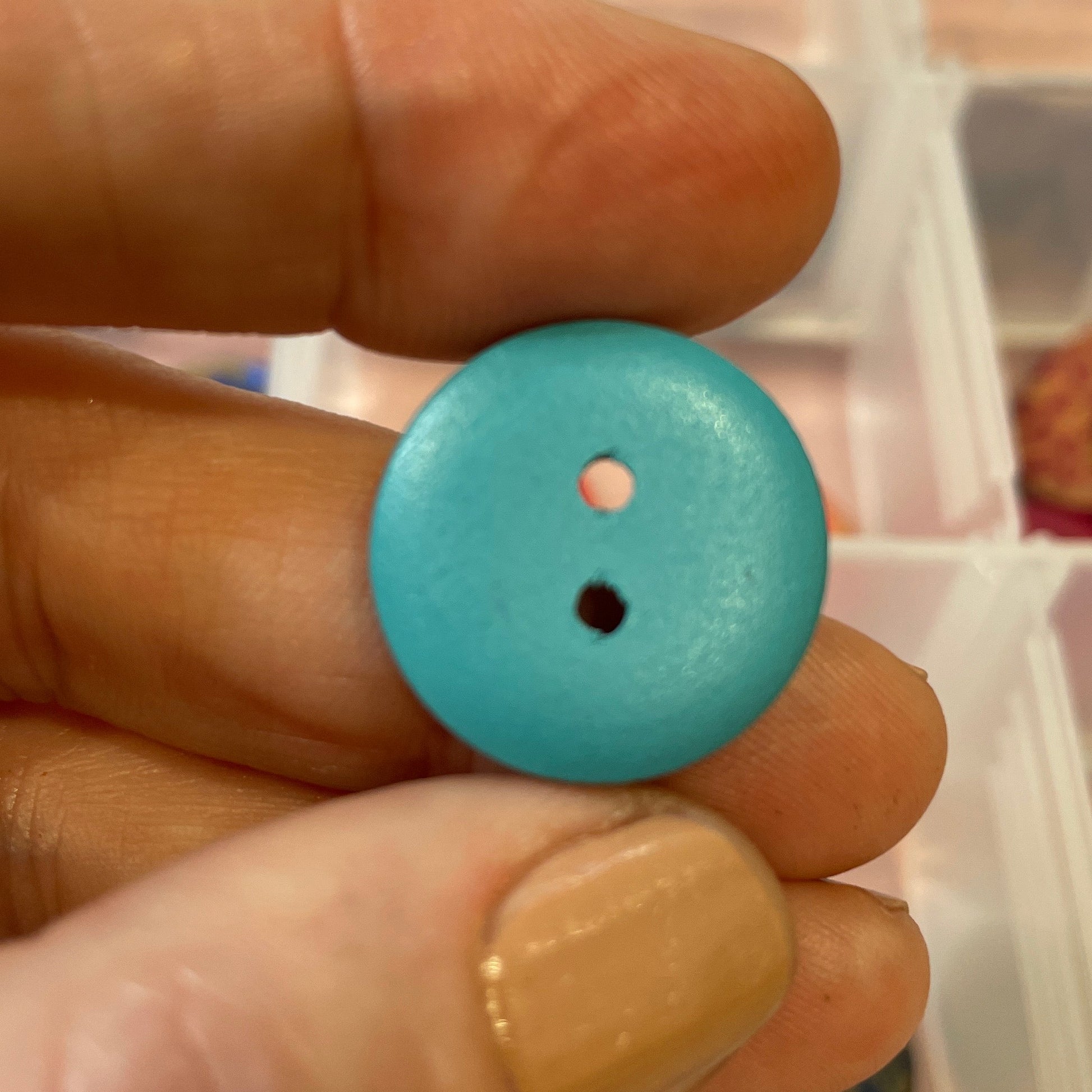 Hand holding a blue button with a clear container of buttons in the background