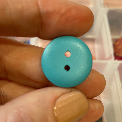 Hand holding a blue button with a clear container of buttons in the background