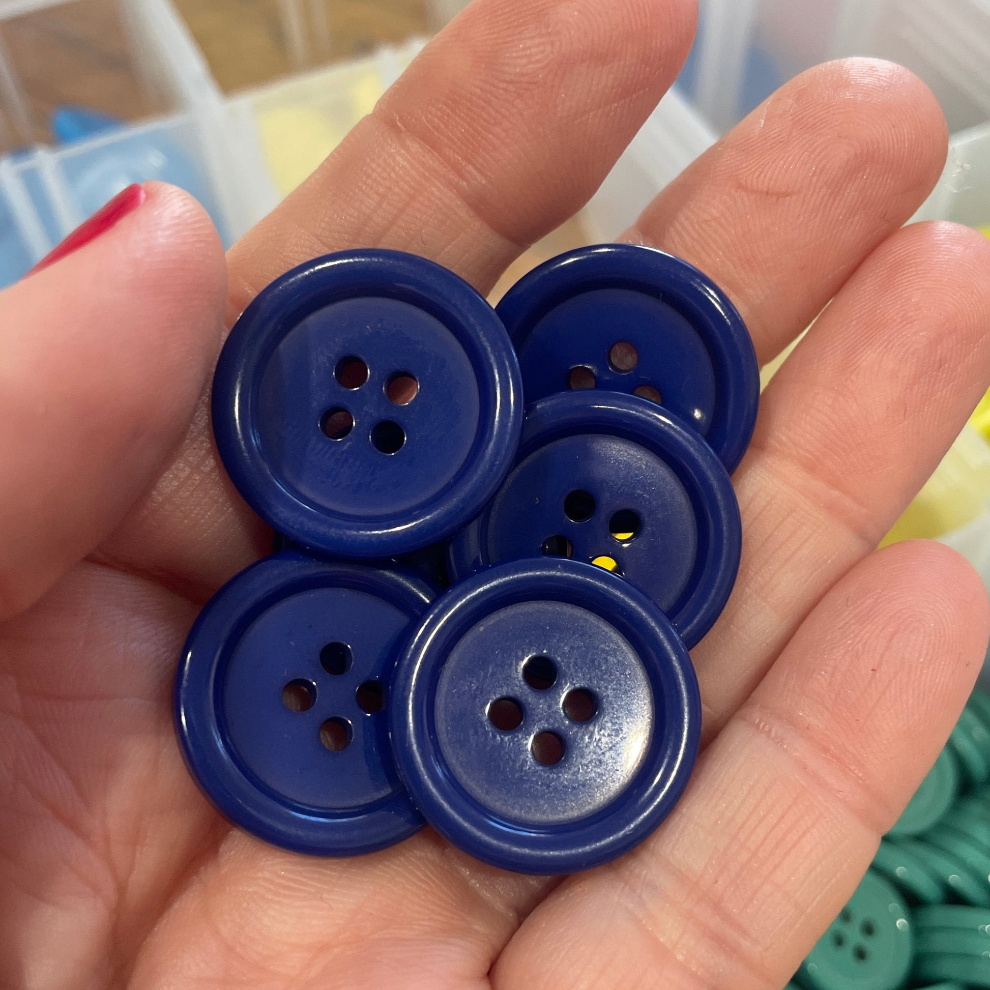 Hand holding blue buttons with a container of buttons in the background