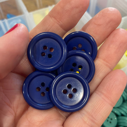 Hand holding blue buttons with a container of buttons in the background