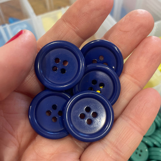 Hand holding blue buttons with a container of buttons in the background