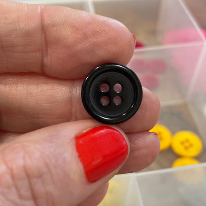 Hand holding a black button with a container of colorful buttons in the background