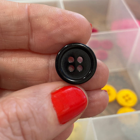 Hand holding a black button with a container of colorful buttons in the background
