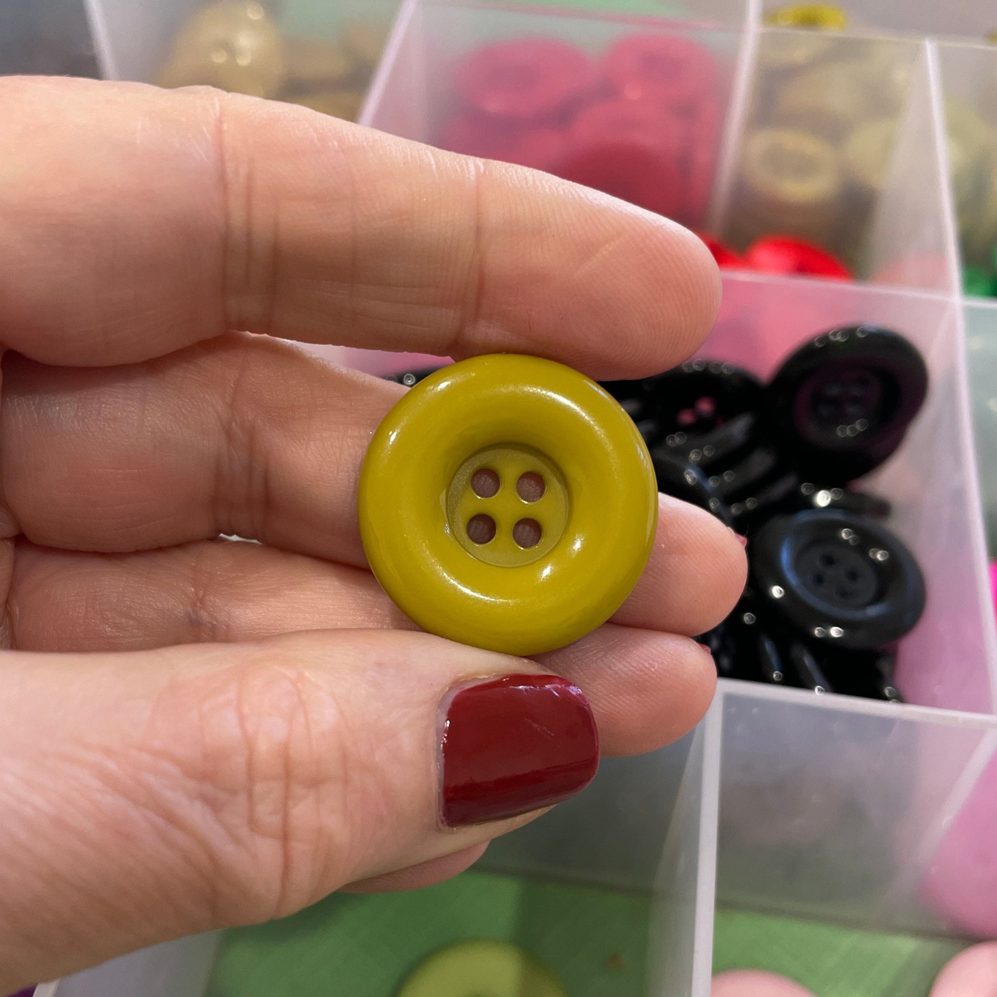 Hand holding a yellow button with a background of assorted buttons in a container