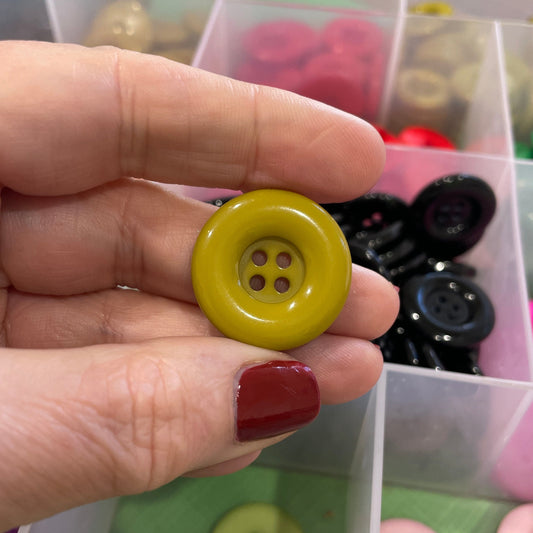 Hand holding a yellow button with a background of assorted buttons in a container