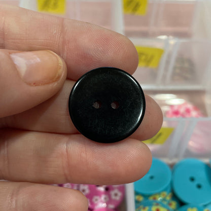 Black button held between fingers with a colorful button collection in the background