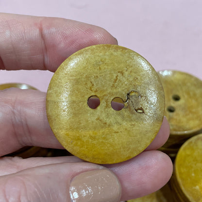 Hand holding a yellow button with more buttons on a pink surface