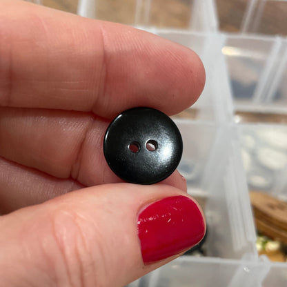 Black button held between fingers with a container of buttons in the background