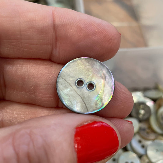 Hand holding a decorative button with a collection of buttons in the background