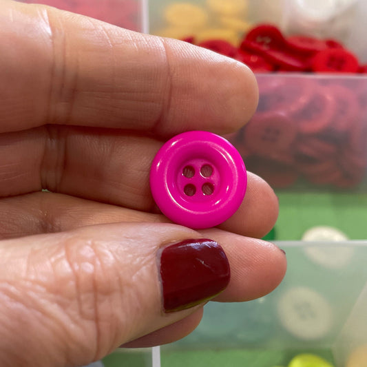 Hand holding a pink button with a container of colorful buttons in the background