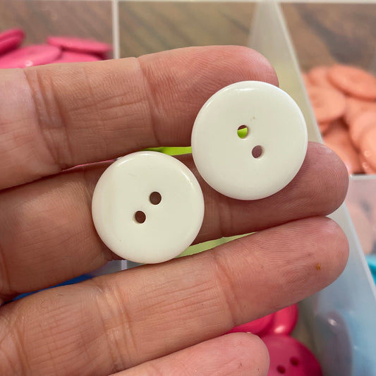 Two white buttons held between fingers with a colorful button collection in the background.