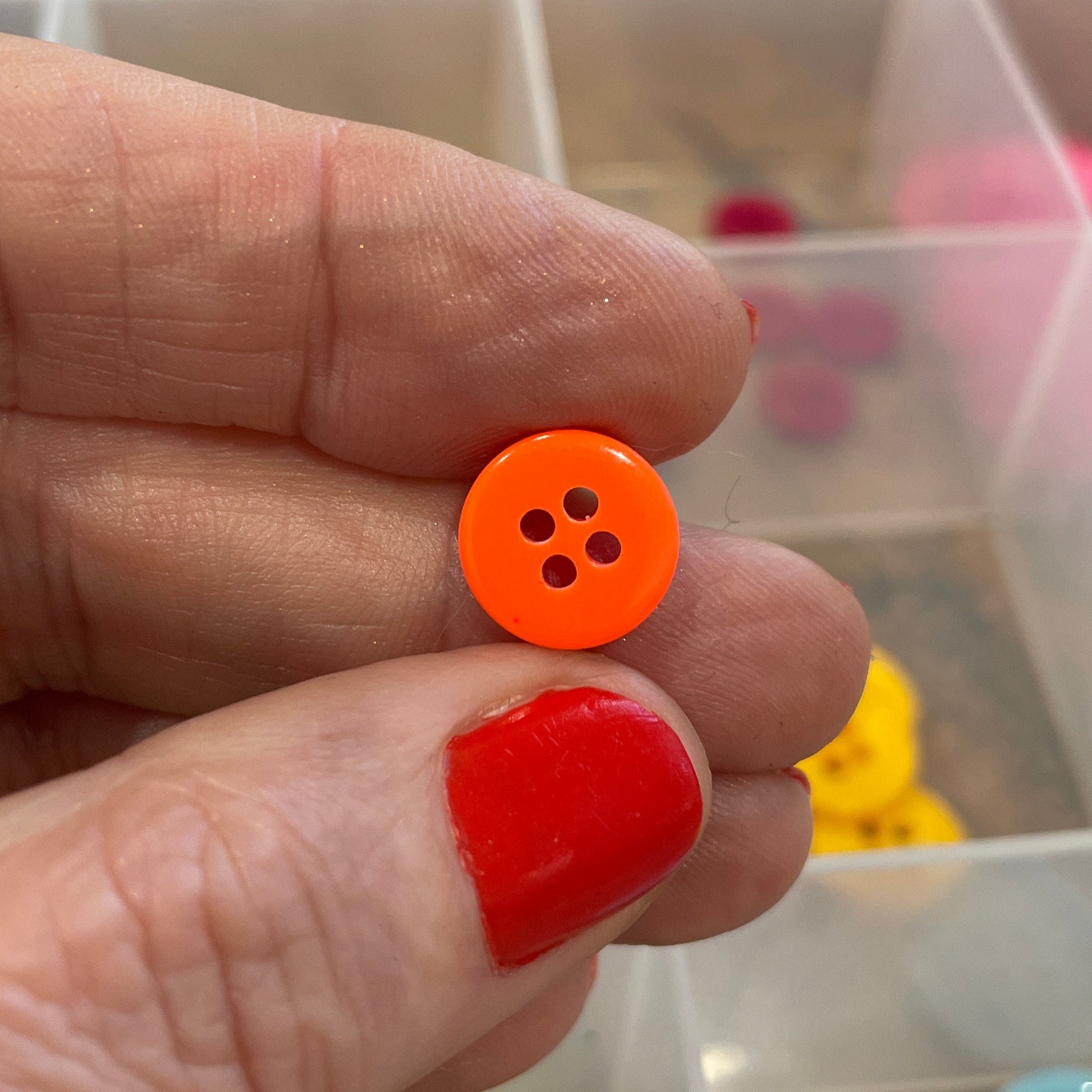 Hand holding two buttons in front of a container with more buttons.
