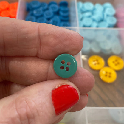 Hand holding a green button with a clear container of colorful buttons in the background