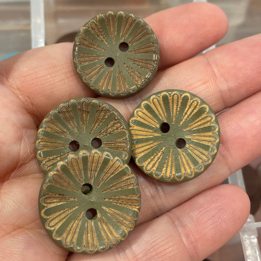 Hand holding three bronze-colored buttons with a clear container of buttons in the background