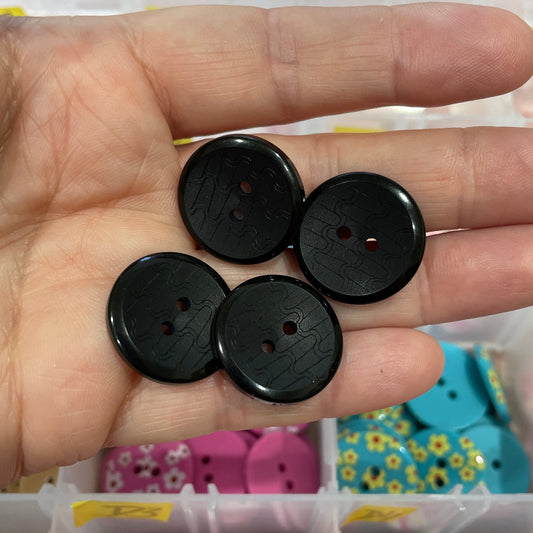 Black buttons held in a hand with a container of colorful buttons in the background