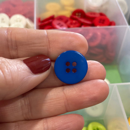 Hand holding a blue button with a container of colorful buttons in the background
