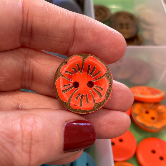 Hand holding a decorative button with a colorful design, against a background of various buttons.
