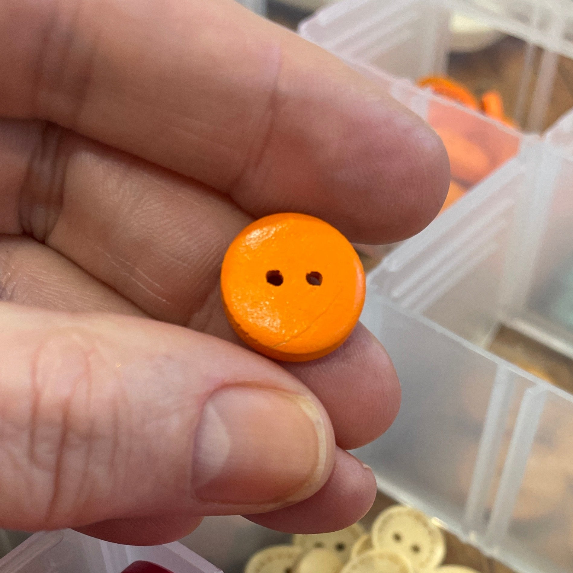 Hand holding an orange button with a container of assorted buttons in the background