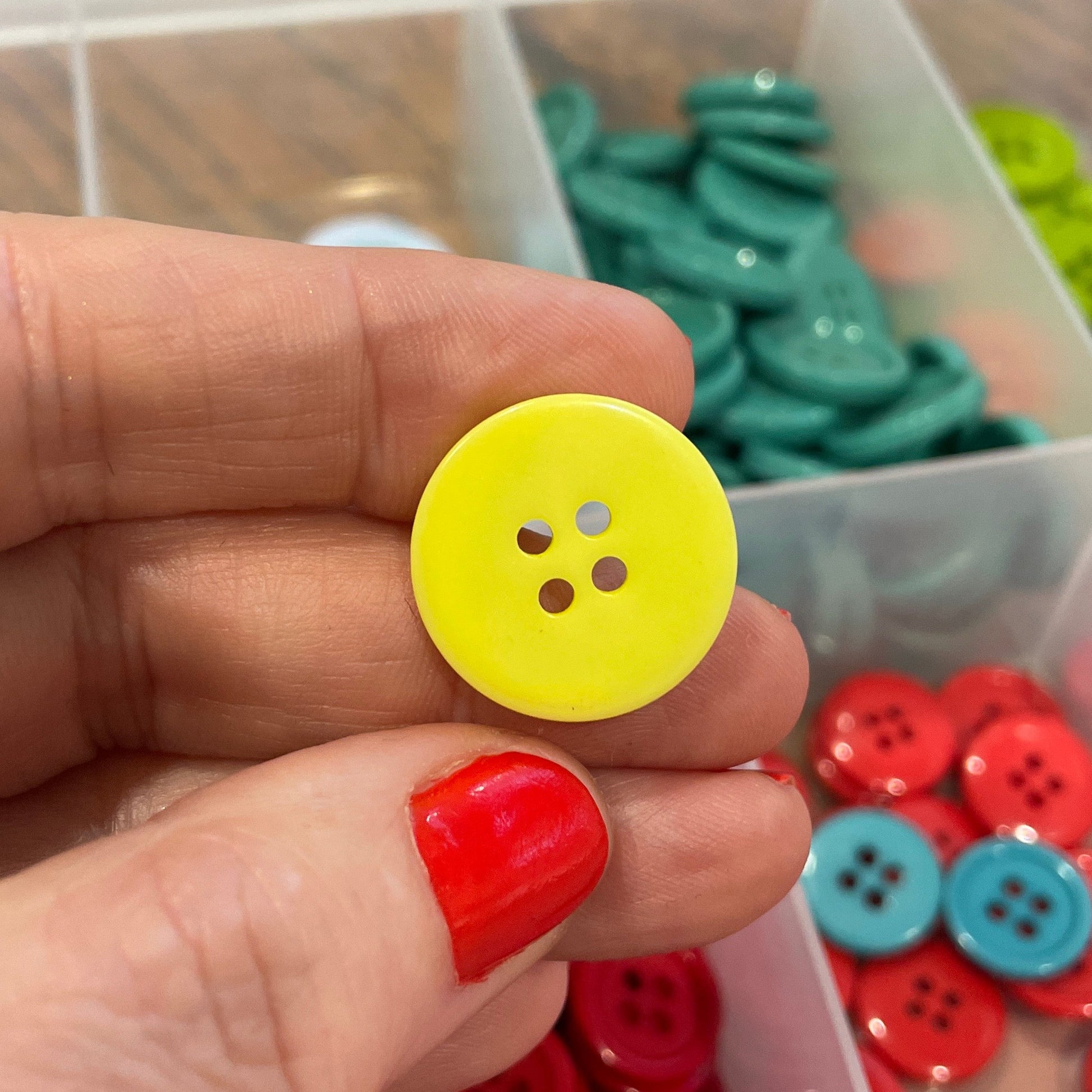 Hand holding a yellow button with a container of colorful buttons in the background