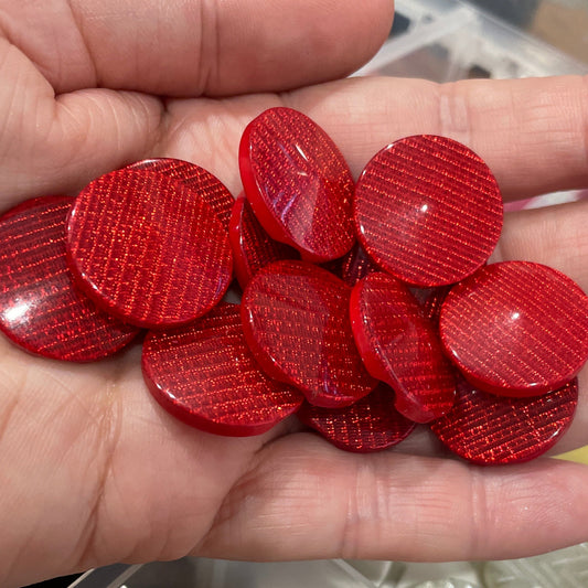 Hand holding red circular objects with a container of various items in the background