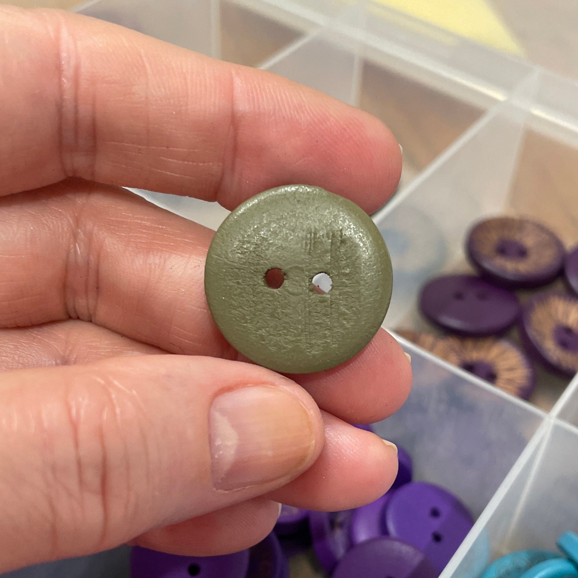 Hand holding a green button with a container of buttons in the background