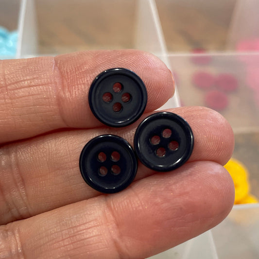 Three black buttons held between fingers with a container of buttons in the background