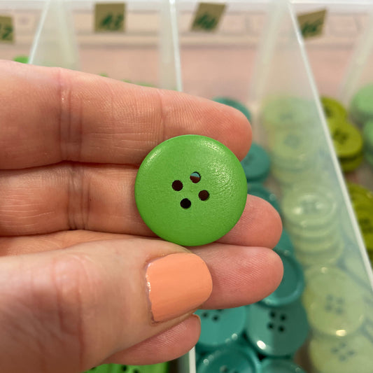 Green button held in a hand with a container of green buttons in the background