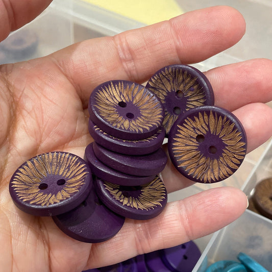 Hand holding purple buttons with a container of blue and purple buttons in the background.