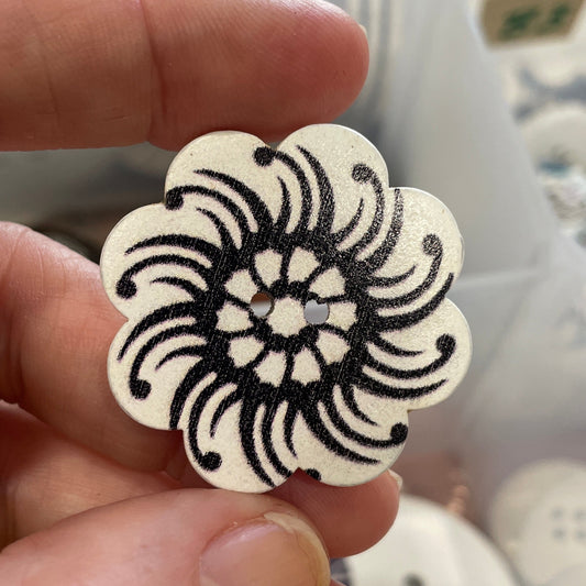 Hand holding a decorative button with a black floral pattern against a blurred background of similar buttons.