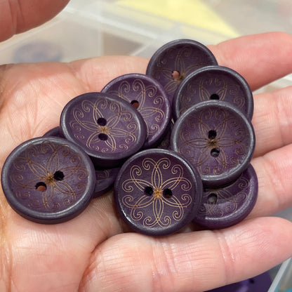 Hand holding purple buttons with a container of blue and purple buttons in the background.