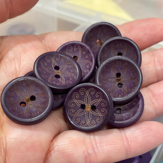 Hand holding purple buttons with a container of blue and purple buttons in the background.