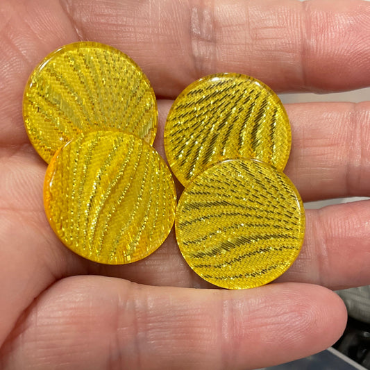 Hand holding three gold circular embellishments with a container of colorful embellishments in the background.