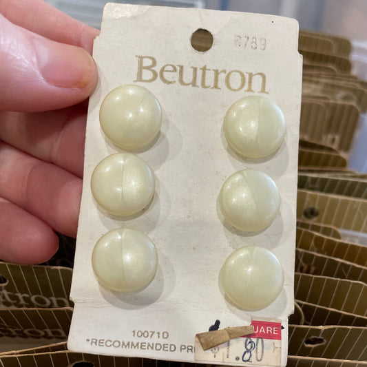 Packaged buttons with a hand holding the packaging, set against a blurred background.