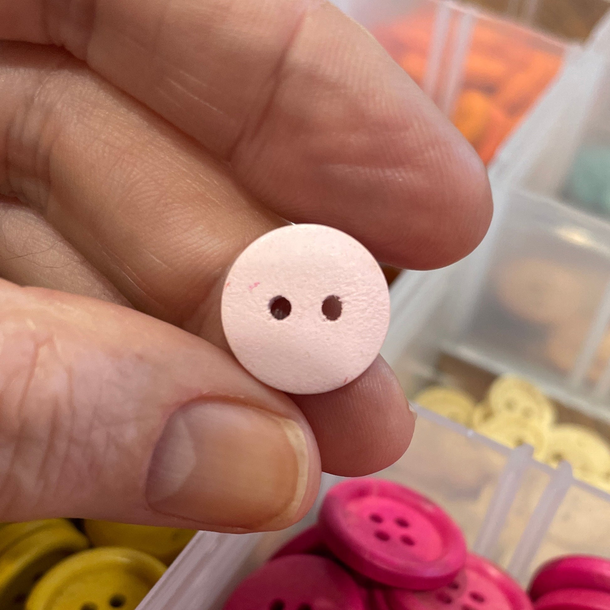 Pink button held by a hand with a container of buttons in the background