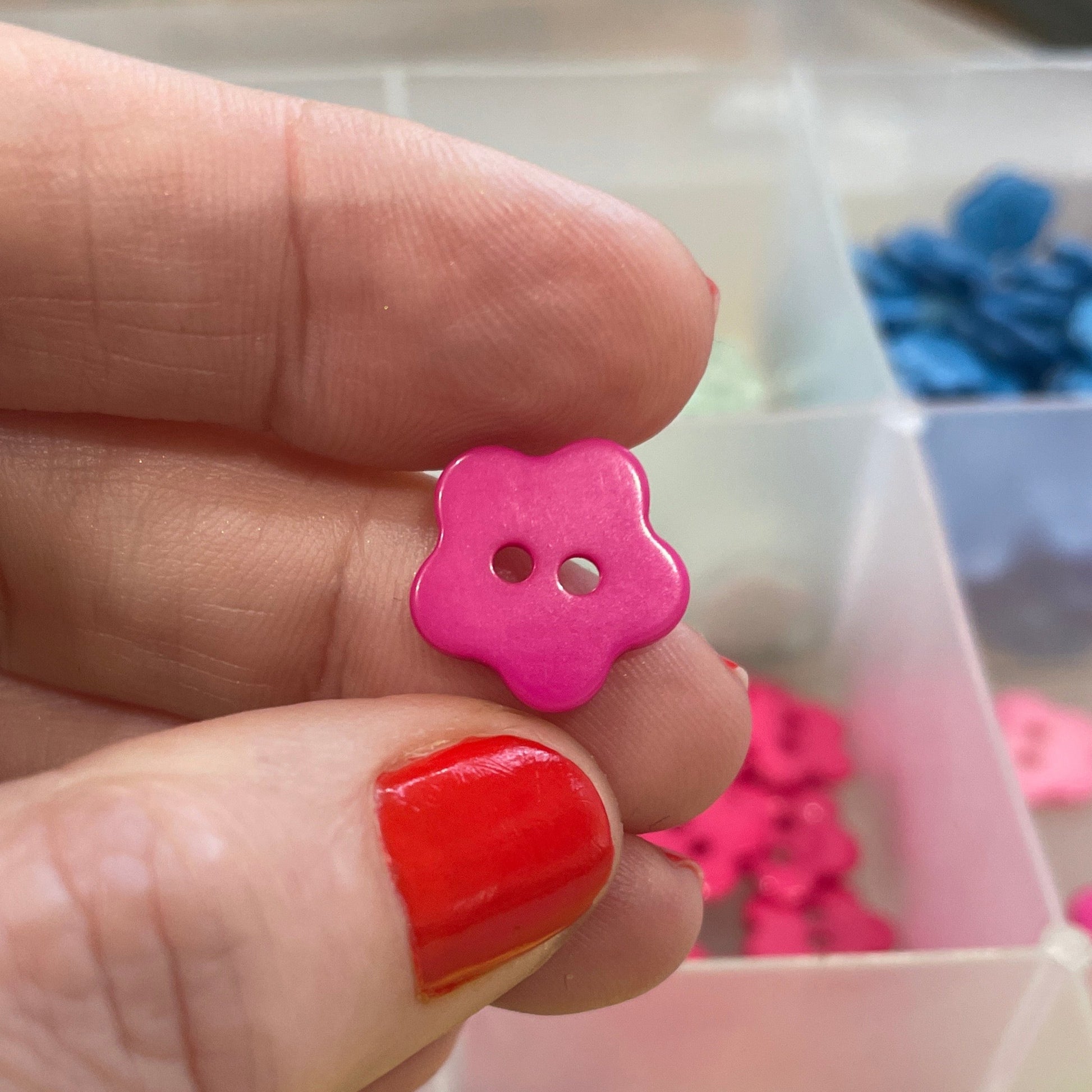 Hand holding a pink flower-shaped button with a blurred background of colorful buttons.